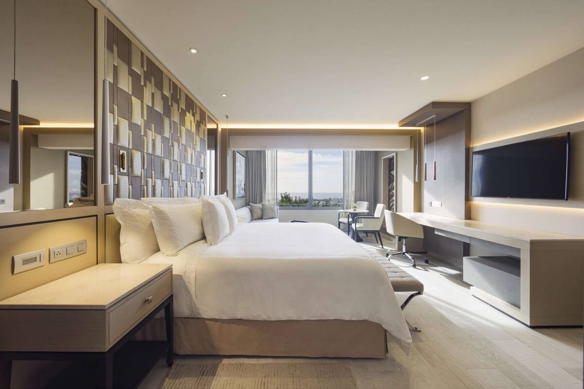 Ein modernes Hotelzimmer mit einem großen Bett, einem Schreibtisch, einem Fernseher und Blick auf die Stadt.