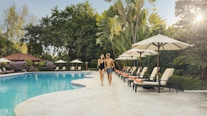 A swimming pool with lounge chairs and umbrellas, surrounded by lush greenery.
