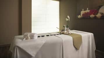 Un cuarto de spa con una camilla de masaje, velas y un espejo decorativo.
