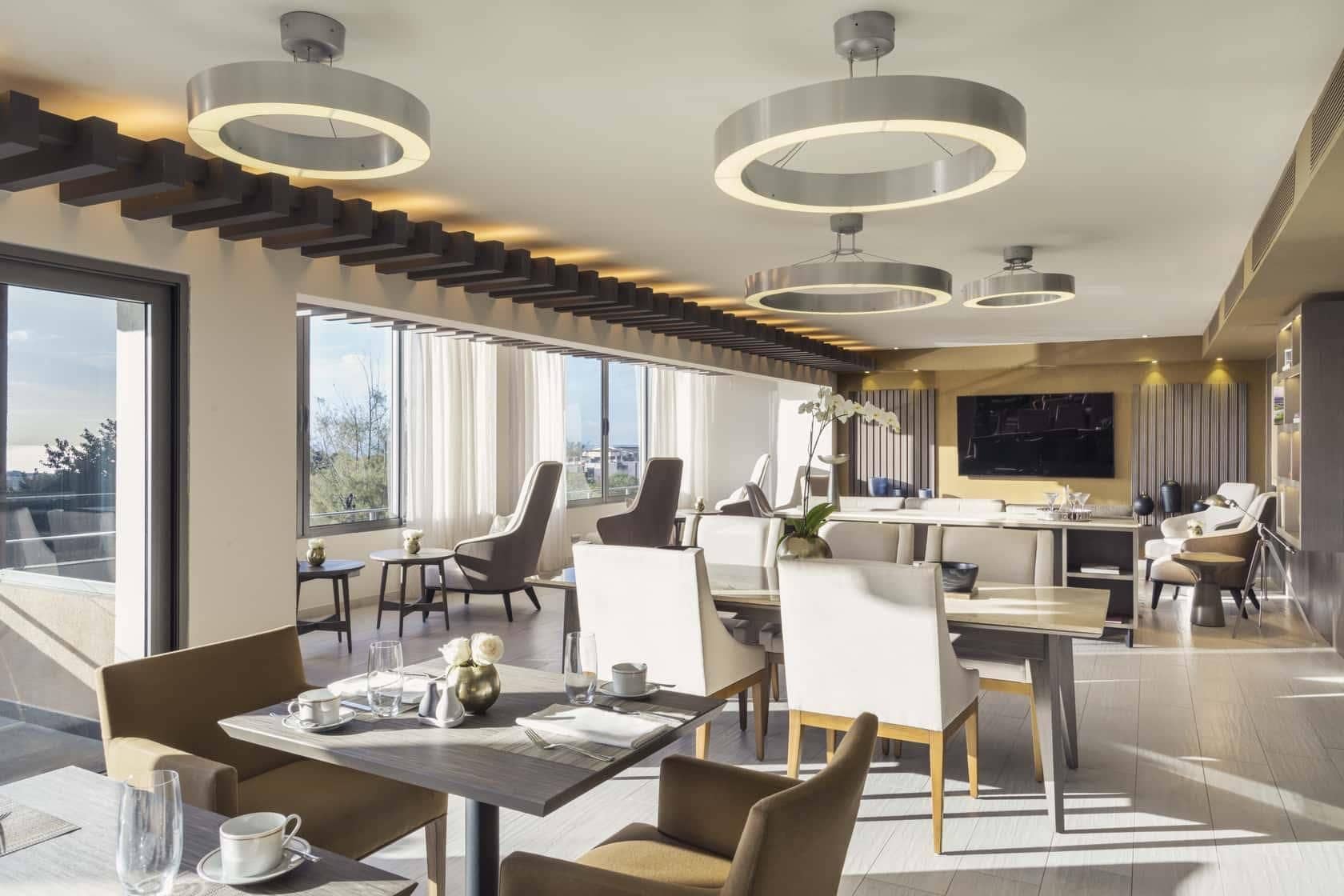 Un comedor moderno con techos altos, lámparas circulares y grandes ventanales que ofrecen vistas al exterior.