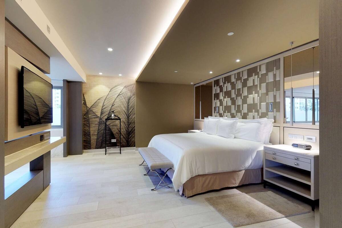 Ein modernes Schlafzimmer mit einem großen Bett, Nachttischen, einem Fernseher und einer Wanddekoration.