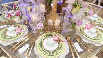 Una mesa redonda dispuesta con platos, cubiertos y cristalería, rodeada de velas y flores.