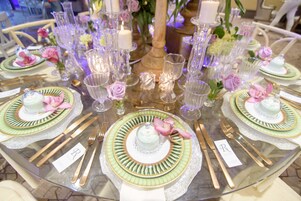 Una mesa redonda dispuesta con platos, cubiertos y cristalería, rodeada de velas y flores.