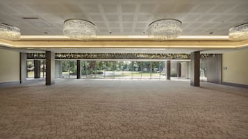 A spacious hall with patterned carpet, large chandeliers, and a view of greenery outside.