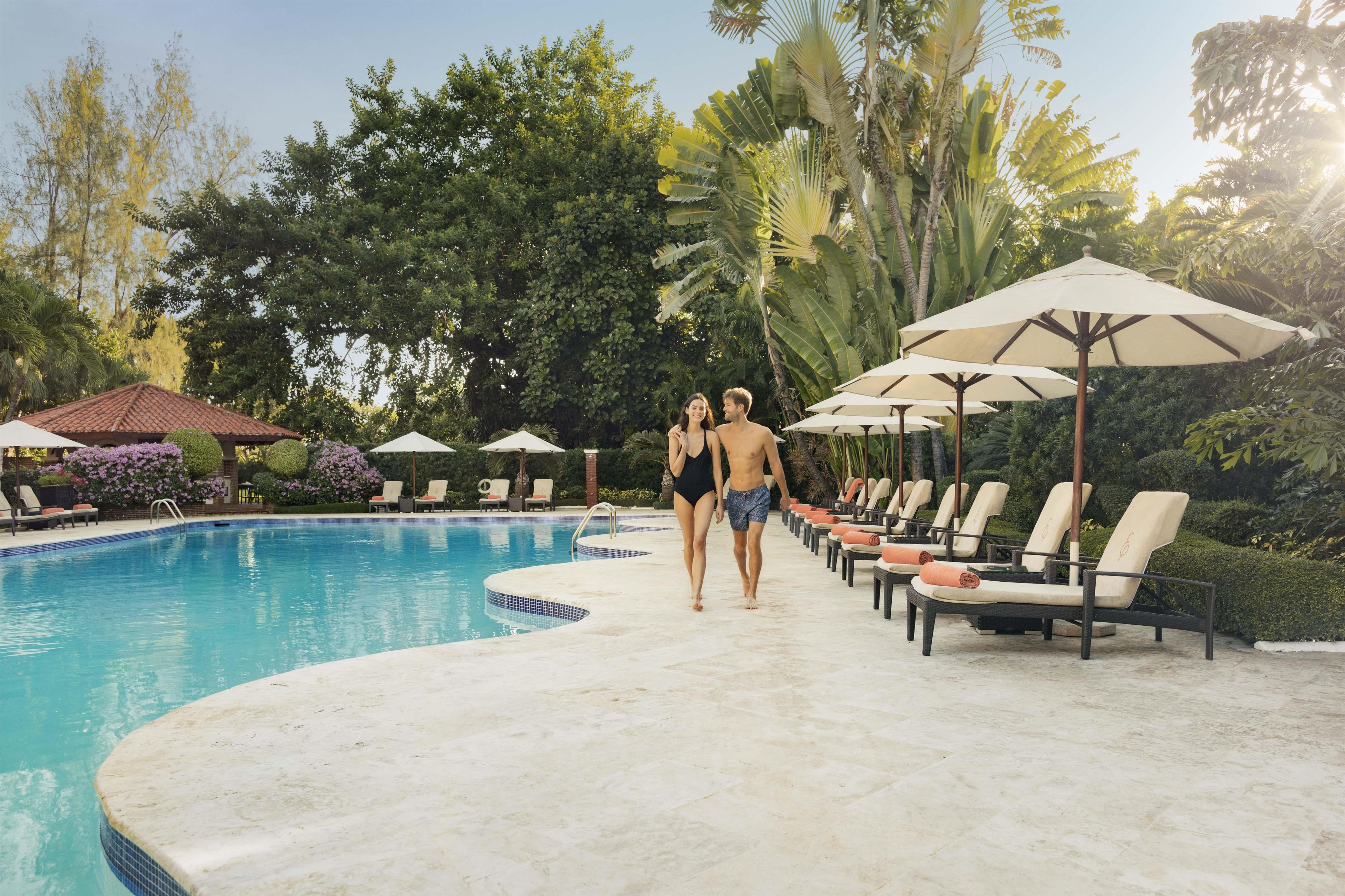 Piscina com espreguiçadeiras e guarda-sóis, cercada por vegetação exuberante.