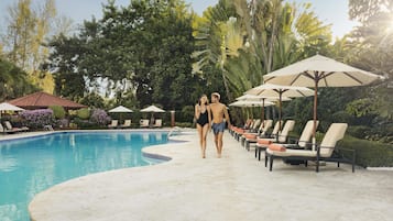 Piscina com espreguiçadeiras e guarda-sóis, cercada por vegetação exuberante.
