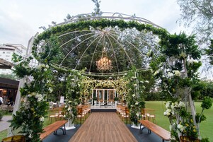Montaje de boda al aire libre con pasillo de madera, arcos florales y una araña.
