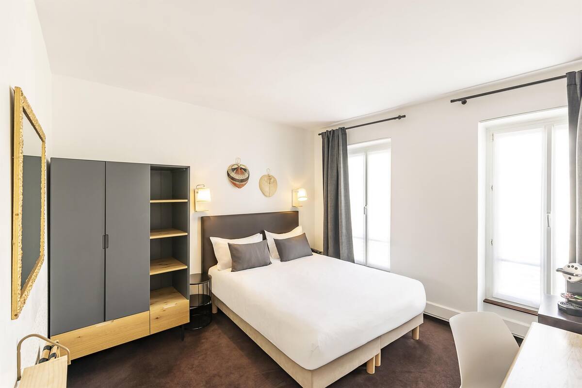 A hotel room with a bed, a wardrobe, a desk, and a chair.