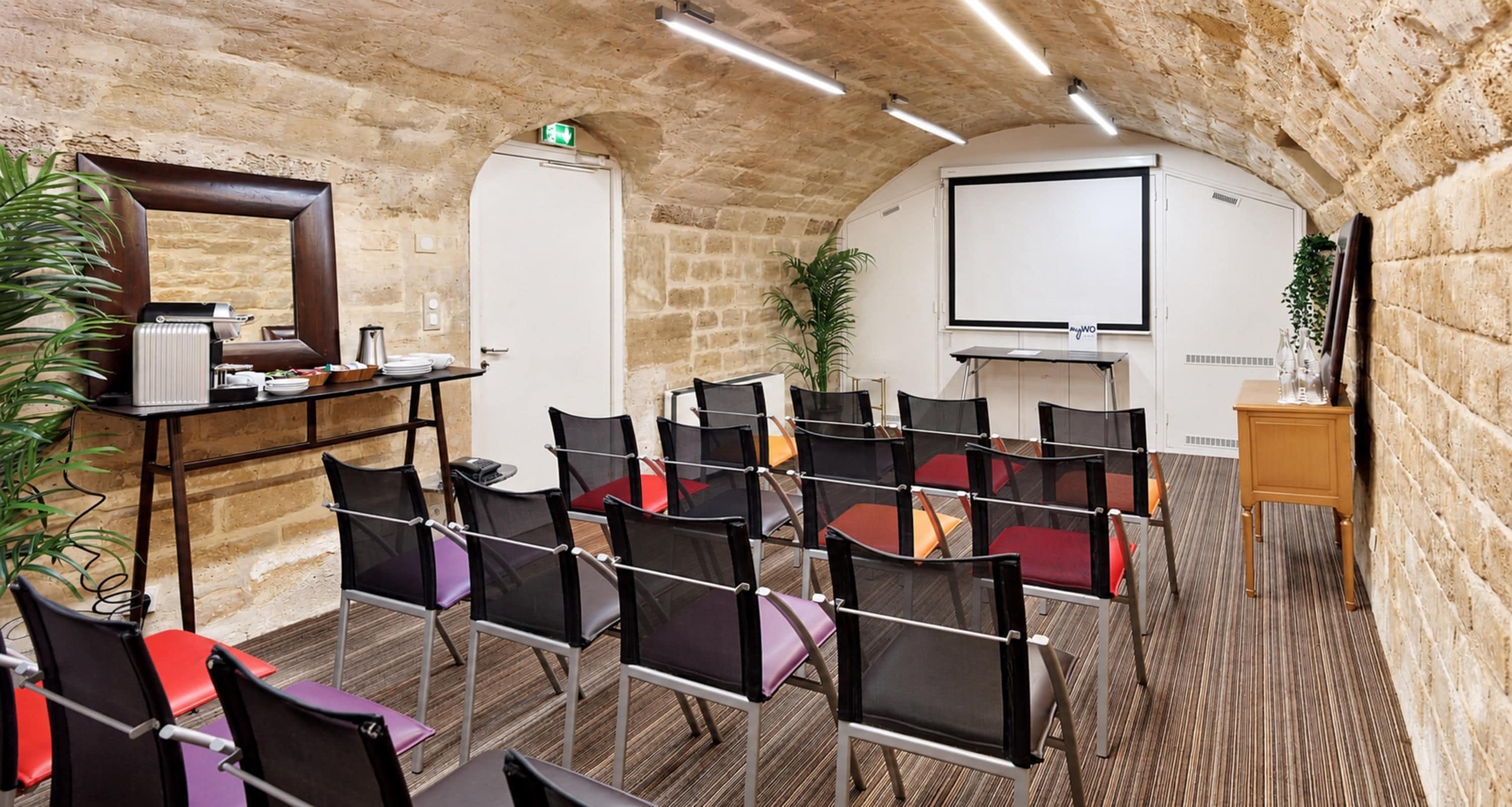 Uma sala de conferências com parede de pedra, tela de projetor e um espaço para café.