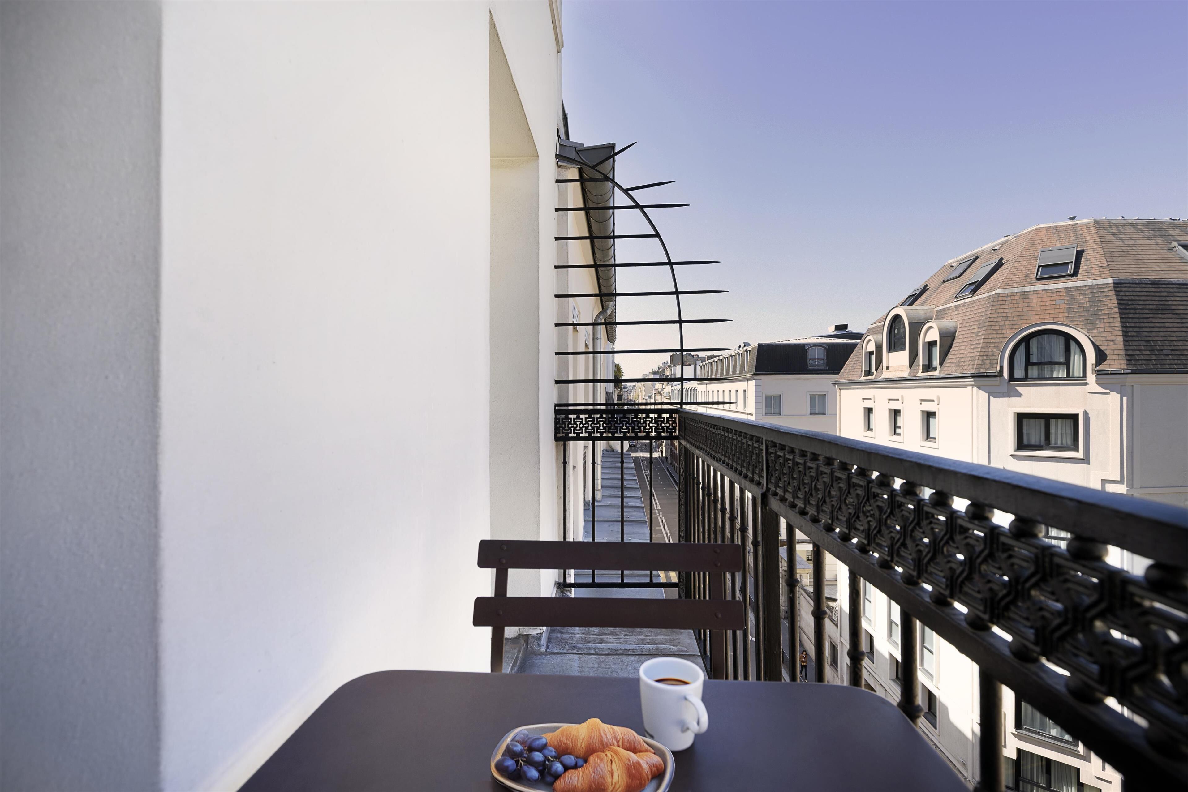 Een balkon met een tafel, een bankje, een croissant en een kop koffie.
