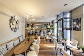 A modern restaurant interior with a long wooden table, white chairs, and a bar area in the background. - Best Western Aramis Saint-Germain (Paris)