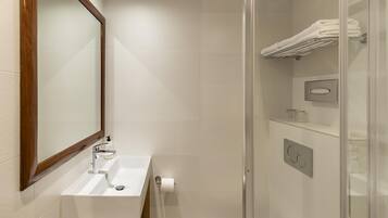 Un baño moderno con lavamanos blanco, espejo y cabina de ducha con mampara de vidrio.