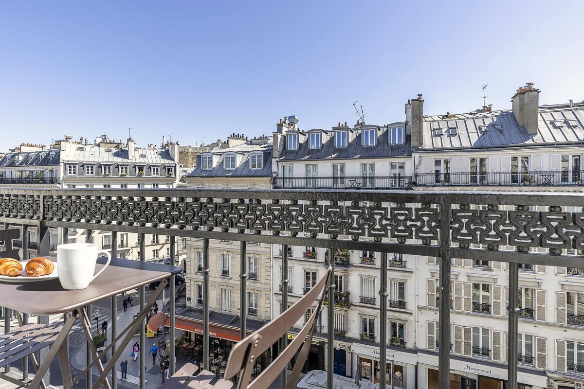 A balcony with a table, chairs, and a view of Parisian buildings.