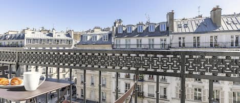 A balcony with a table, chairs, and a view of Parisian buildings.