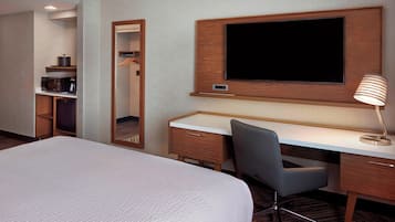A hotel room with a large bed, a desk with a chair, a flat-screen TV mounted on the wall, a mirror, and a lamp.