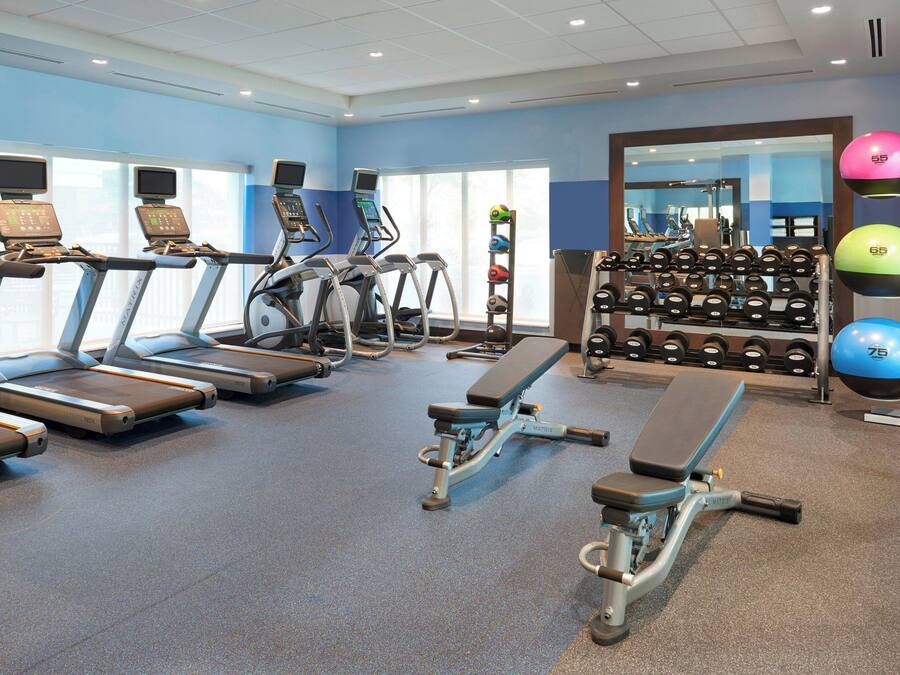Et fitnesscenter med løbebånd, crosstrainere, en bænk og et stativ med håndvægte.