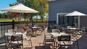 An outdoor patio area with tables and chairs, umbrellas, and a view of trees and a building. - Four Points by Sheraton Hamilton - Stoney Creek (Hamilton)