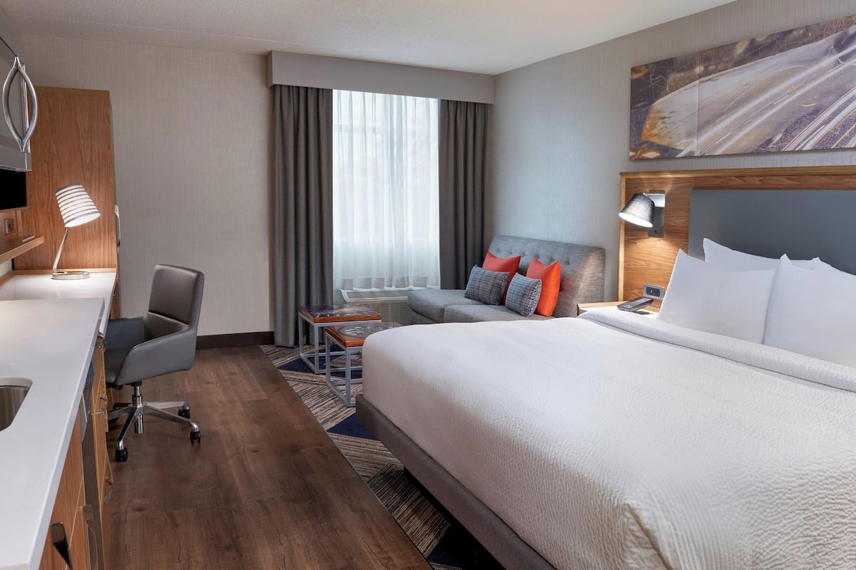 A hotel room with a large bed, a desk with a lamp, a chair, a small table, and a TV.