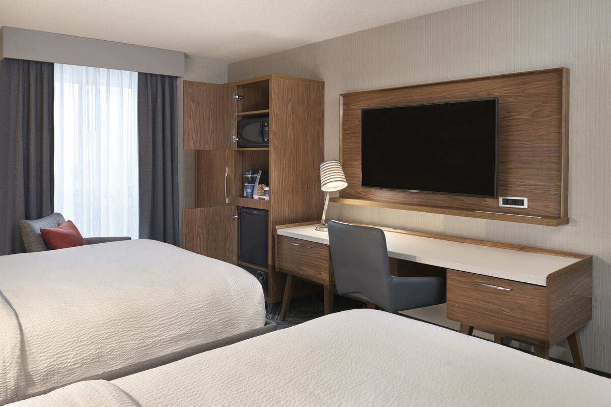 A hotel room with two beds, a desk with a computer, a television, and a wardrobe.