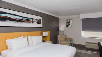 A hotel room with a large bed, a desk, a chair, a lamp, and artwork on the walls.