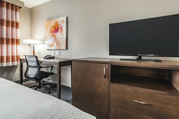 Una habitación de hotel con una cama, un escritorio con una silla, un televisor y un armario.
