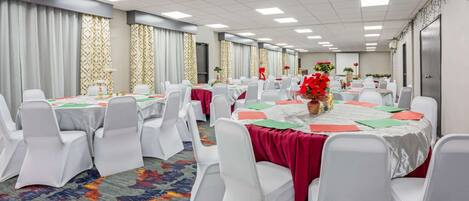 Un salón de conferencias con varias mesas, sillas blancas y piso alfombrado.