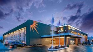 A hotel with a prominent sun logo, multiple flags, and a parking lot with vehicles. - La Quinta Inn & Suites by Wyndham Seattle Federal Way (Federal Way)