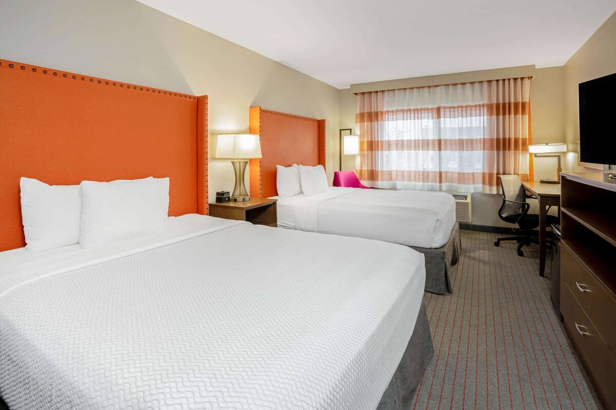 A hotel room with two beds, a desk, a chair, a television, and a window with curtains.