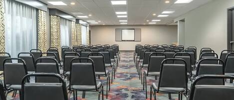 A conference room with rows of chairs, a projector screen, and patterned curtains.