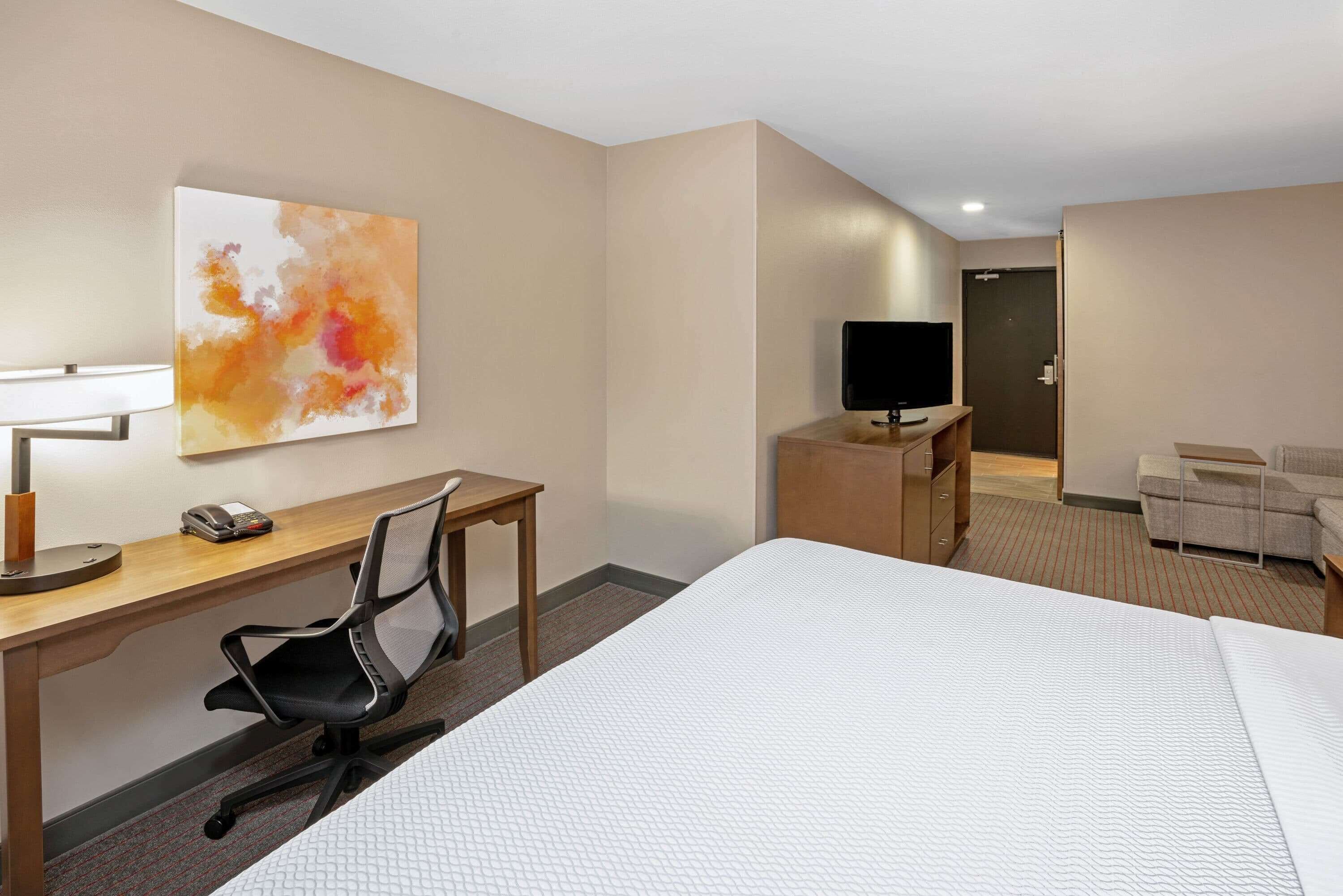 Una habitación de hotel con cama, escritorio, silla, televisión y obras de arte en la pared.