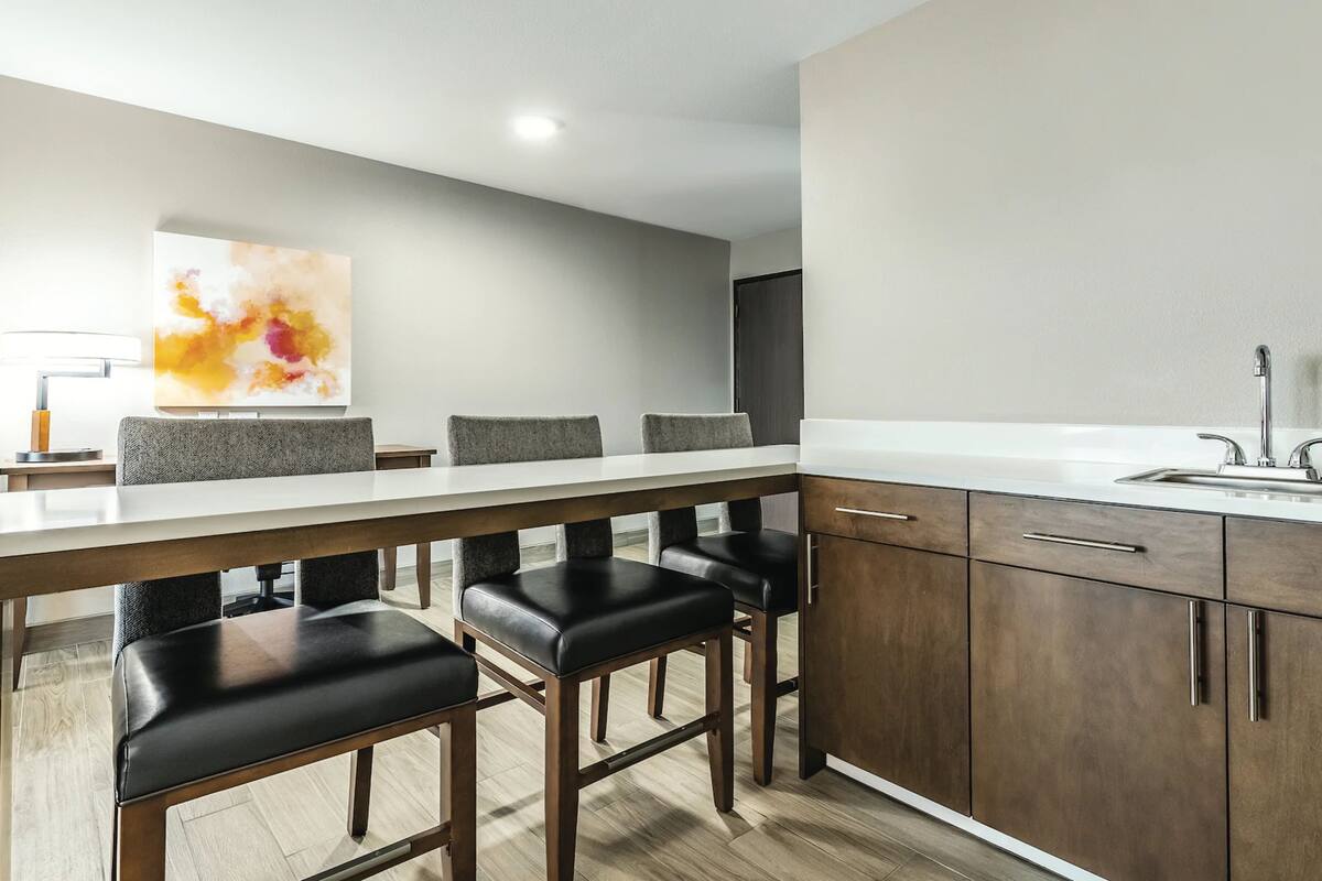A modern kitchen with a long counter, bar stools, and a large painting on the wall.