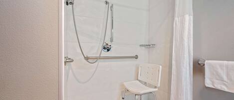 A shower area with a grab bar, a white chair, and a showerhead.