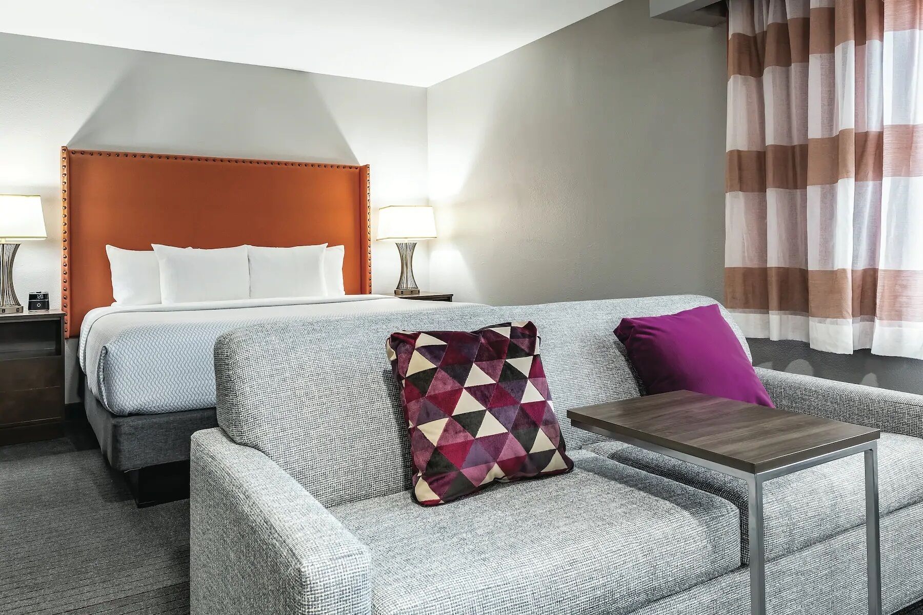 Une chambre d’hôtel avec un lit double, un canapé, une petite table et une table de chevet avec une lampe.