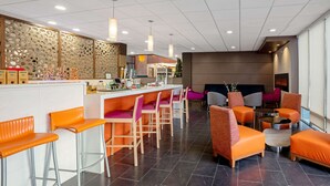 A modern hotel lobby with a reception desk, bar area, and seating with orange and gray chairs. - La Quinta Inn & Suites by Wyndham Seattle Federal Way (Federal Way)