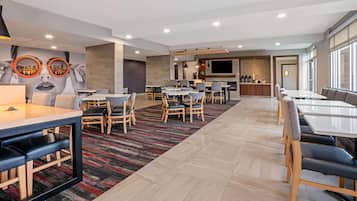 A modern hotel lobby with multiple seating areas, a bar, and a large TV screen.
