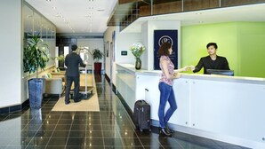 Un espace d’accueil d’hôtel au design moderne, comprenant un comptoir d’accueil, un espace d’attente avec des sièges et un escalier en arrière-plan.