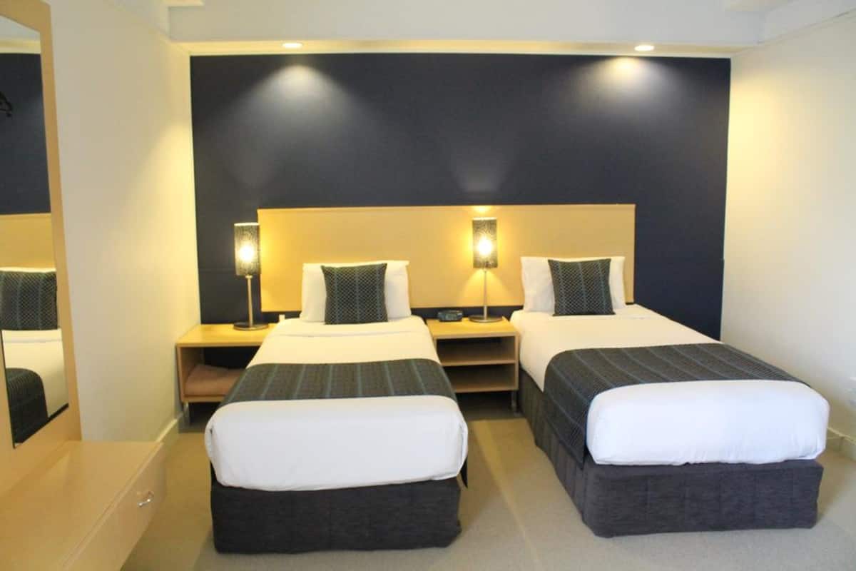 A hotel room with two single beds, a desk, and a mirror.