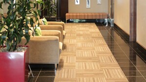 Un hall d’hôtel doté d’un tapis à motifs, d’un espace salon, de plantes en pot et d’un mur en verre.