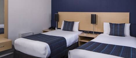 A hotel room with two beds, each with a headboard and bedside tables. There is a small bedside table with a lamp and a phone on one side.