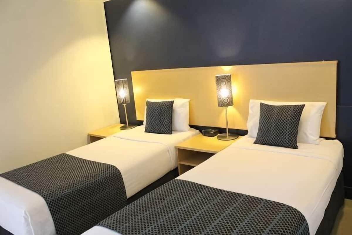 A hotel room with two beds, each with a headboard, bedside tables, lamps, and pillows.