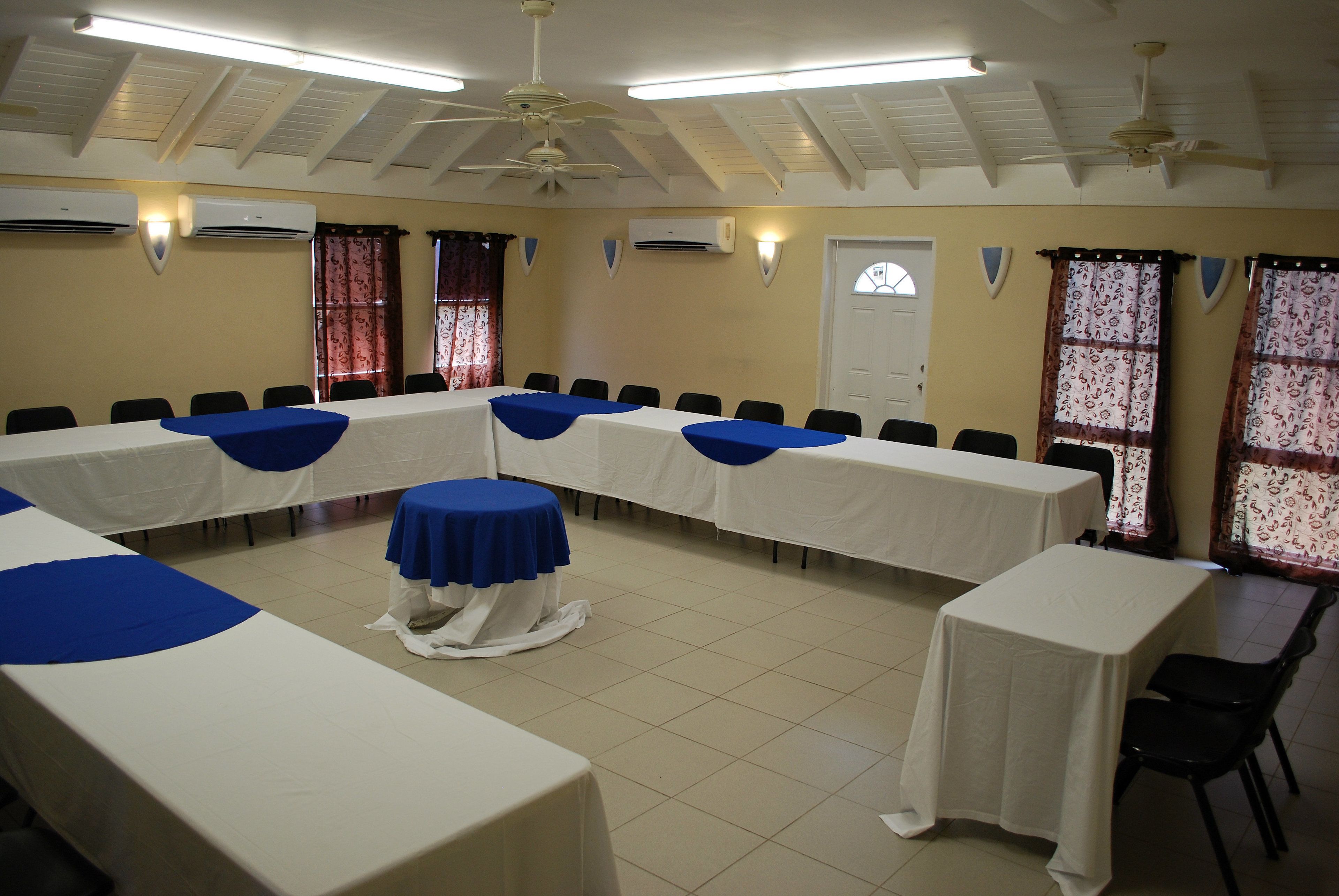 Un salón de conferencias con mesas blancas, manteles azules y sillas negras.