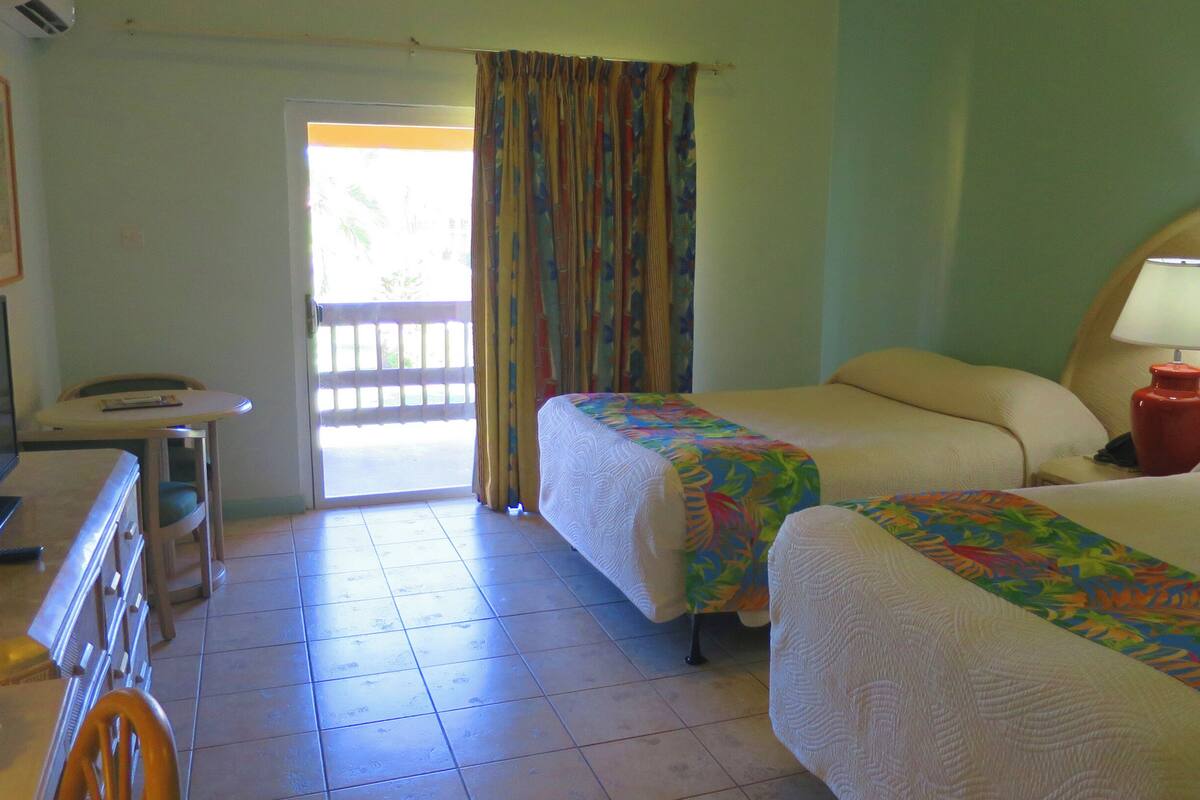 A hotel room with two beds, a desk with a computer, a chair, and a balcony with a view.