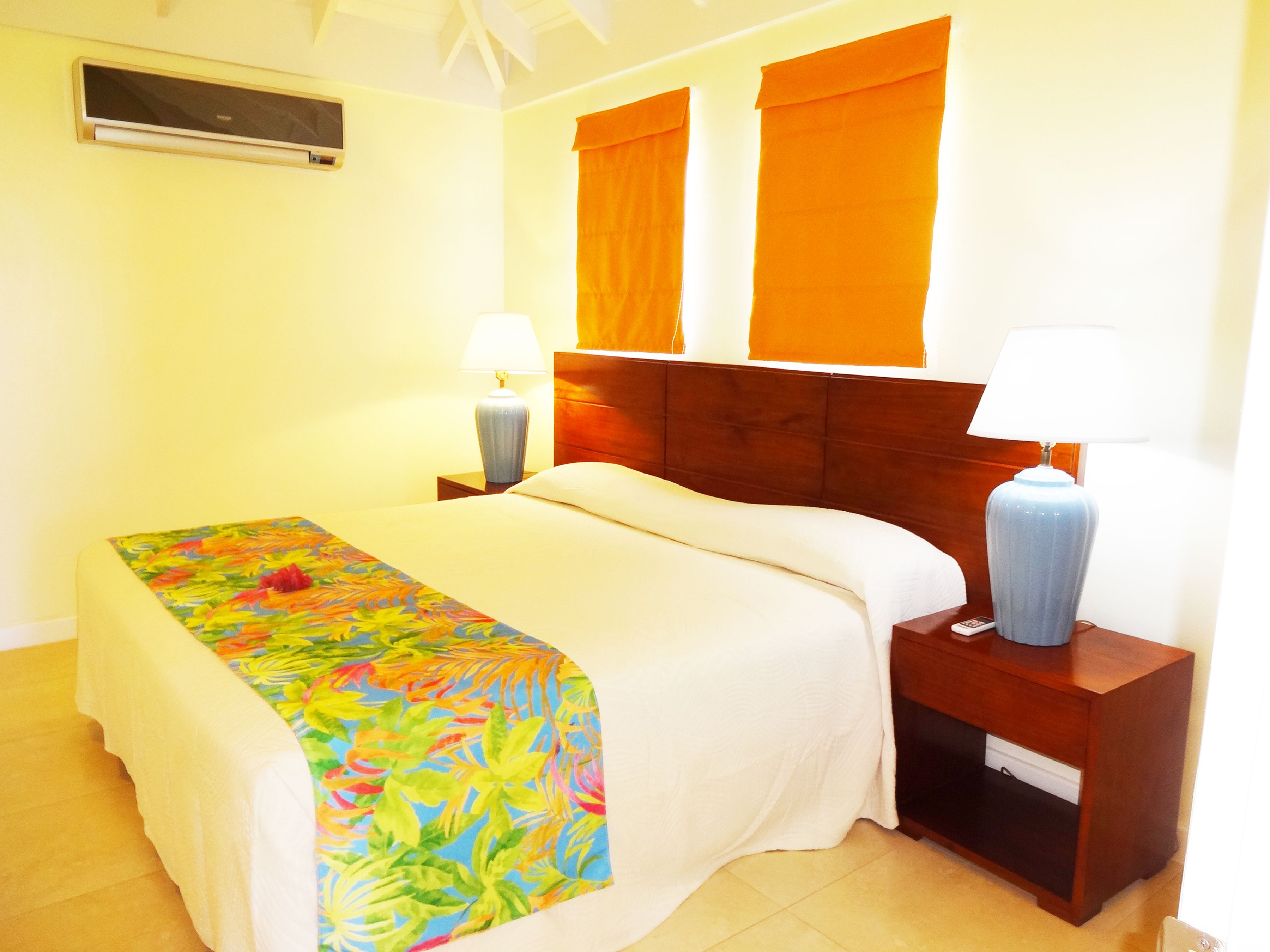 Habitación de hotel con cama, dos mesitas de noche, una ventana con cortinas naranjas y un ventilador de techo.