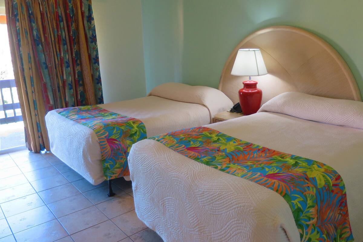 A hotel room with two beds, each with a colorful floral bedspread, a red bedside lamp, and a large round headboard.