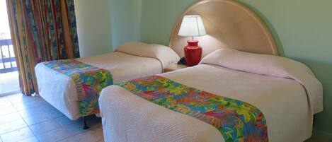 Habitación de hotel con dos camas, cada una con una colcha floral de colores, una lámpara de noche roja y un cabecero grande y redondo.