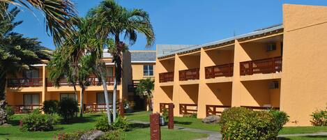 A hotel with multiple floors, outdoor balconies, and a well-maintained garden with palm trees and shrubs.