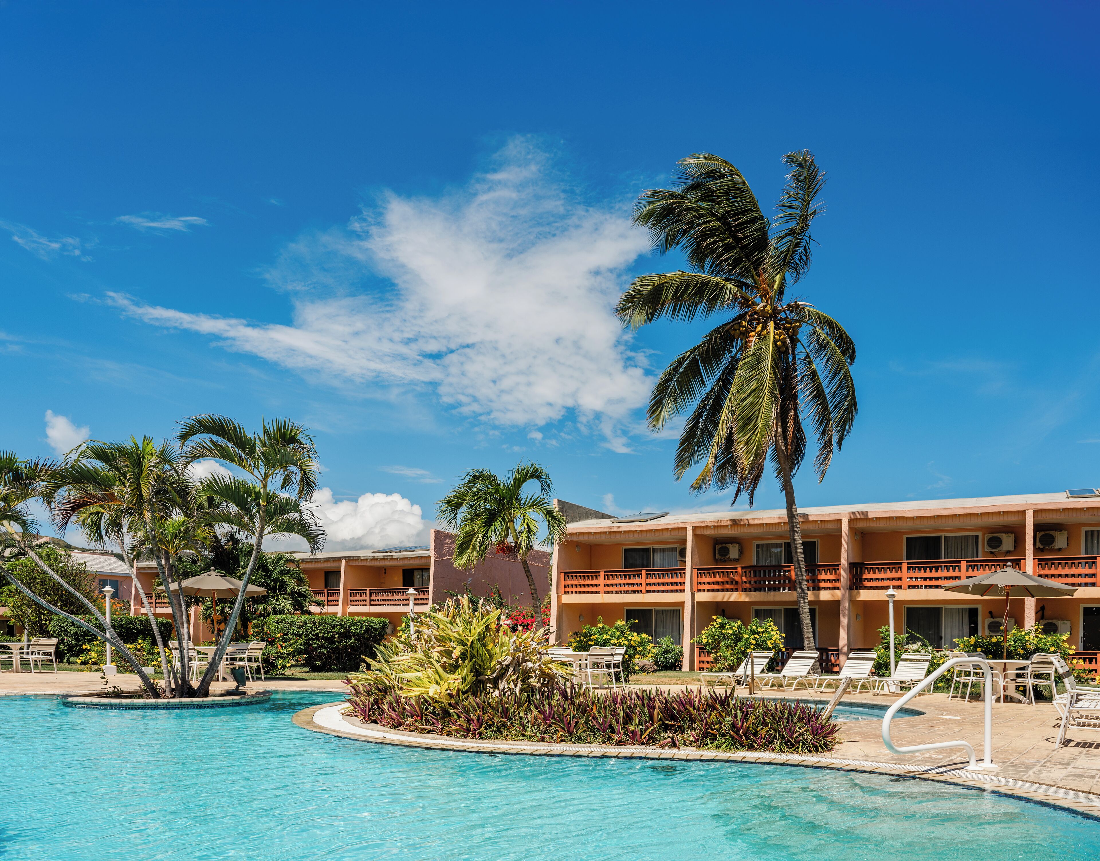 A hotel with a pool, palm trees, and a clear blue sky.