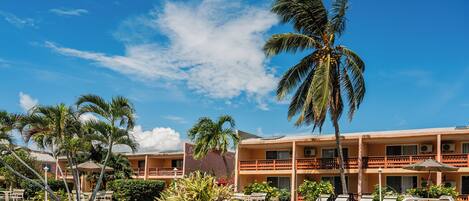 A hotel with a pool, palm trees, and a clear blue sky.