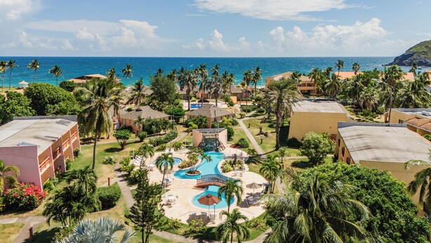 Un resort con varias edificaciones, una piscina central y vista al océano.