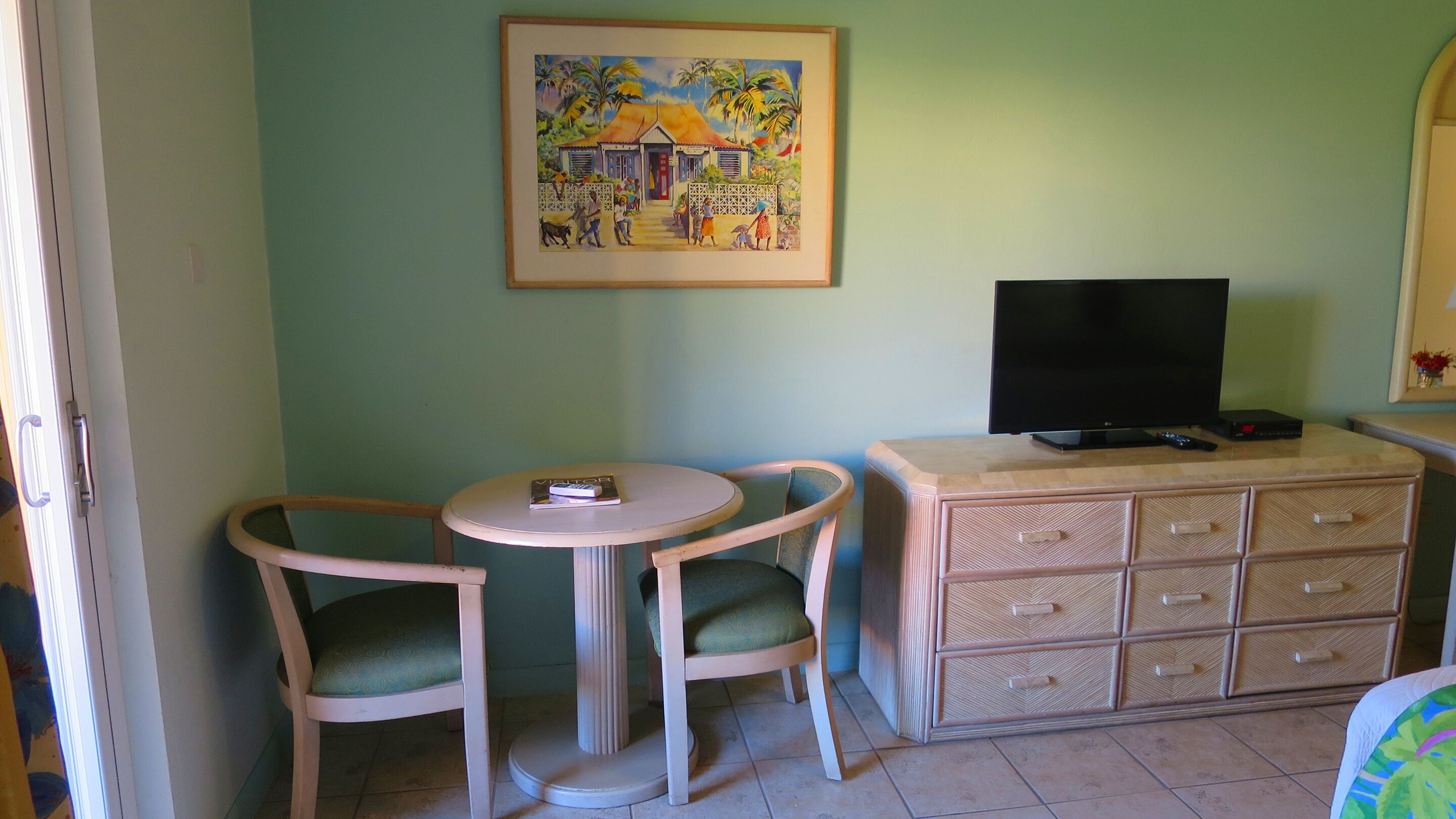 A room with two chairs, a small table, a TV on a cabinet, and a painting on the wall.